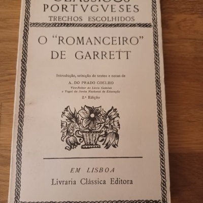 Capa de livro clássico em português com texto e moldura decorativa, sobre fundo de madeira.