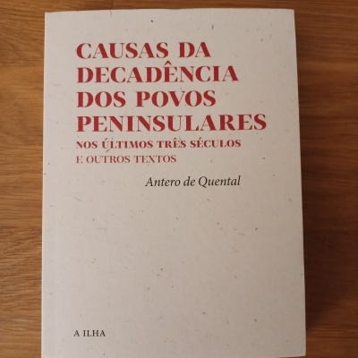 Livro com título CAUSAS DA DECADÊNCIA DOS POVOS PENINSULARES em capa branca sobre mesa de madeira