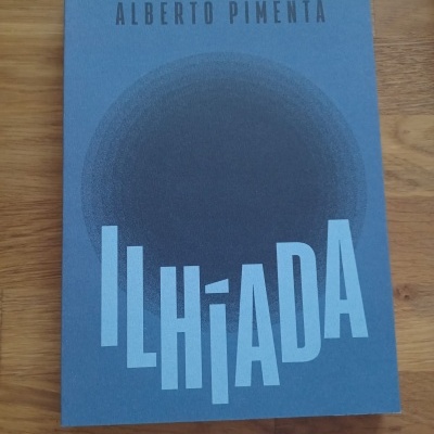 Livro azul ILHÍADA com círculo preto e texto ALBERTO PIMENTA