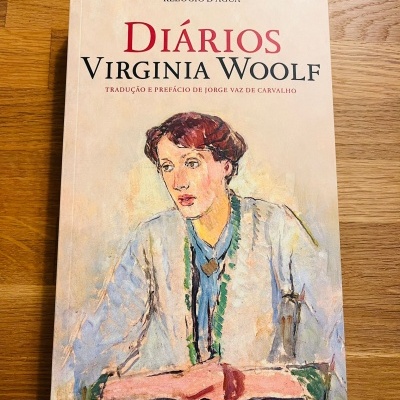 Capa de livro 'Diários Virginia Woolf' com ilustração de mulher, sobre mesa de madeira
