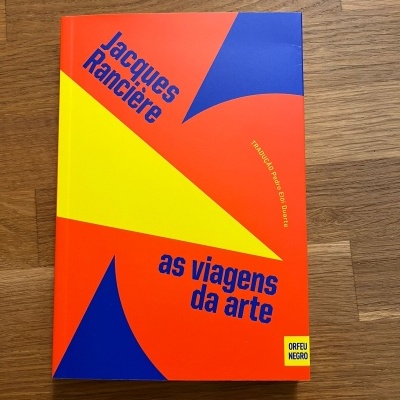 Livro colorido 'as viagens da arte' de Jacques Rancière sobre madeira