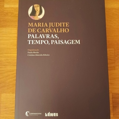 Livro com capa preta, texto em dourado e branco, retrato circular, sobre superfície de madeira.