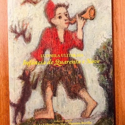 Capa de livro com figura infantil vermelha, tocando cornetinha, e gato preto