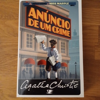 Livro 'ANÚNCIO DE UM CRIME' de Agatha Christie sobre mesa de madeira