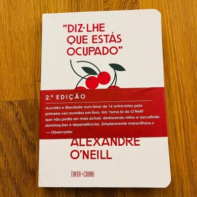 Capa de livro branco com título vermelho, cerejas desenhadas e faixa vermelha com texto