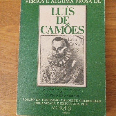 Capa de livro verde com título Versos e Alguma Prosa de Luís de Camões e ilustração em preto e branco do poeta