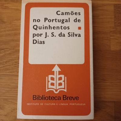 Capa de livro branco e laranja com texto preto sobre madeira clara