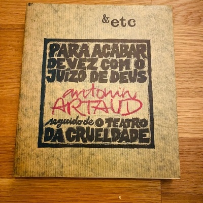 Capa de livro bege envelhecido com texto preto e vermelho sobre madeira clara