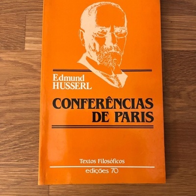 Capa de livro laranja com texto Conferências de Paris, autor Edmund Husserl e ilustração de rosto.