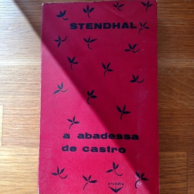 Capa de livro vermelho com texto e estampas pretas sobre uma mesa de madeira clara