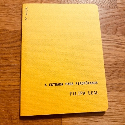 Livro amarelo com título e autor em texto preto numa mesa de madeira