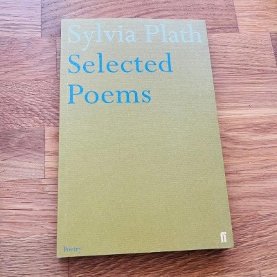 Livro verde-oliva 'Sylvia Plath Selected Poems' sobre superfície de madeira