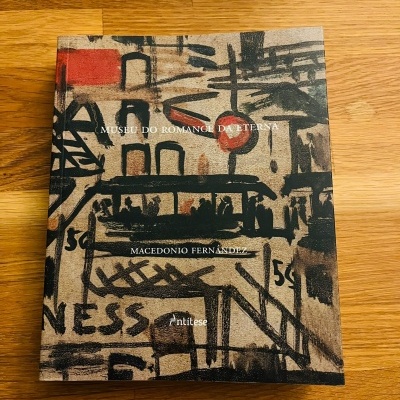 Livro com capa ilustrada com grafismos e texto em cima de mesa de madeira