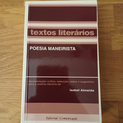 Capa de livro em bordô e rosa com texto sobre poesia maneirista, sobre superfície de madeira clara