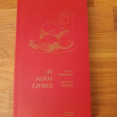 Livro vermelho com texto dourado AS MÃOS LIVRES, mesa de madeira