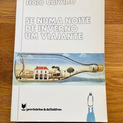 Capa de livro com ilustração de edifício dentro de garrafa sobre mesa de madeira