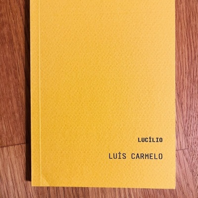 Livro com capa amarela e textos 'LUCÍLIO' e 'LUÍS CARMELO' em preto