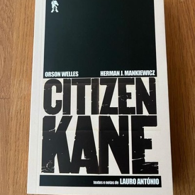 Capa de livro Citizen Kane com texto em preto e branco sobre superfície de madeira.