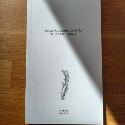 Livro branco com texto preto sobre pintura de Henri Michaux sobre mesa de madeira