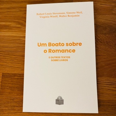 Livro branco com texto laranja e preto numa mesa de madeira