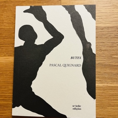 Livro Butes de Pascal Quignard com capa arte em silhueta preta e branca sobre mesa de madeira