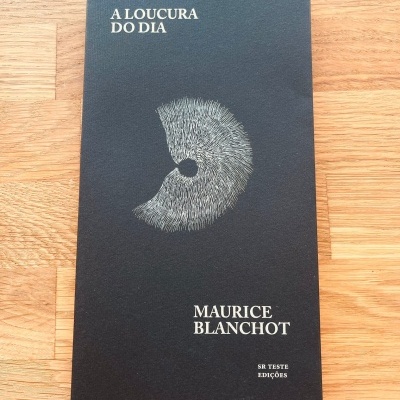 Livro 'A LOUCURA DO DIA' de Maurice Blanchot com capa preta e ilustração branca