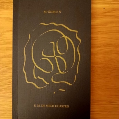 Livro de capa preta com texto e gravura dourada sobre superfície de madeira clara