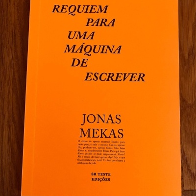 Livro laranja com título e autor em letras pretas colocado sobre madeira.