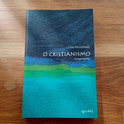 Livro 'O CRISTIANISMO Compreender' de Linda Woodhead com capa azul e verde sobre mesa de madeira
