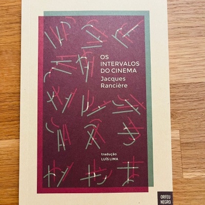 Livro 'OS INTERVALOS DO CINEMA Jacques Rancière' com capa branca e design geométrico em verde e vermelho.
