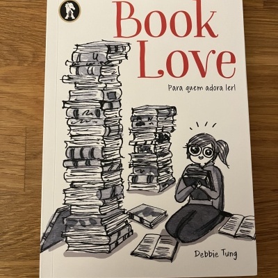Capa de livro 'Book Love' com ilustração a preto de pilhas de livros e personagem a ler em fundo branco