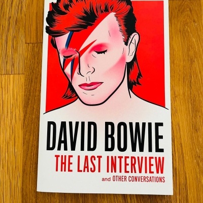 Livro David Bowie com capa ilustrada em fundo vermelho e branco sobre mesa de madeira.