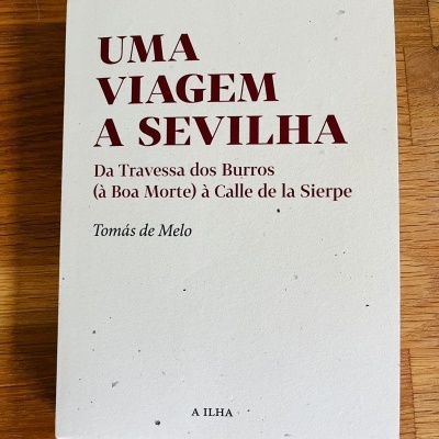 Livro branco 'UMA VIAGEM A SEVILHA' com título e autor em texto vermelho e preto