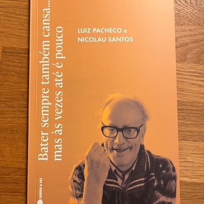 Livro de capa laranja com texto e foto de homem idoso de óculos pretos