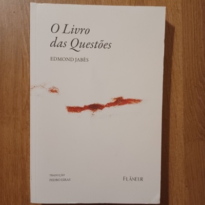 Livro branco com título 'O Livro das Questões' de Edmond Jabès com mancha vermelha