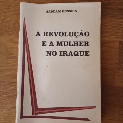 Livro A Revolução e a Mulher no Iraque de Saddam Hussein sobre mesa de madeira