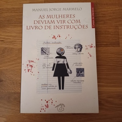 Capa de livro branco com título em vermelho e ilustração feminina preta em fundo de madeira