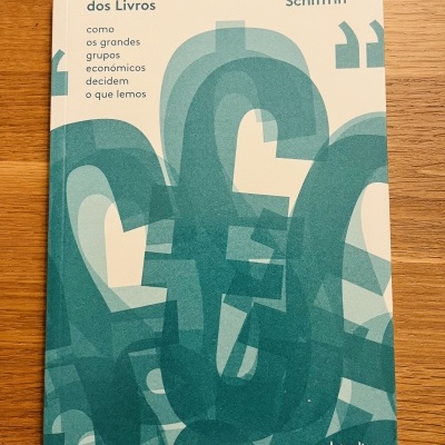 Livro 'O Negócio dos Livros' de André Schiffrin sobre mesa de madeira