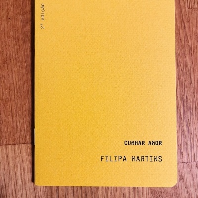 Livro de capa amarela com texto preto sobre piso de madeira