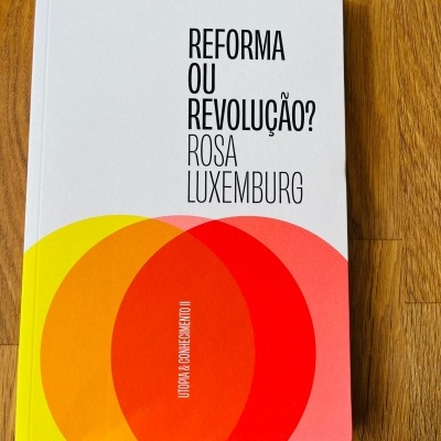 Livro 'REFORMA OU REVOLUÇÃO? ROSA LUXEMBURG' com design de círculos coloridos sobre mesa de madeira.