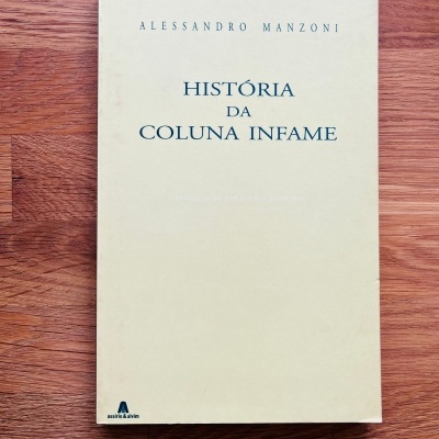 Livro ALESSANDRO MANZONI HISTÓRIA DA COLUNA INFAME com capa bege sobre mesa de madeira
