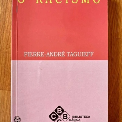 Livro 'O RACISMO' de Pierre-André Taguieff com capa vermelha e rosa sobre superfície de madeira