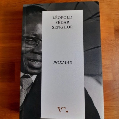 Livro Poemas de Léopold Sédar Senghor com capa preta e branca sobre mesa de madeira.