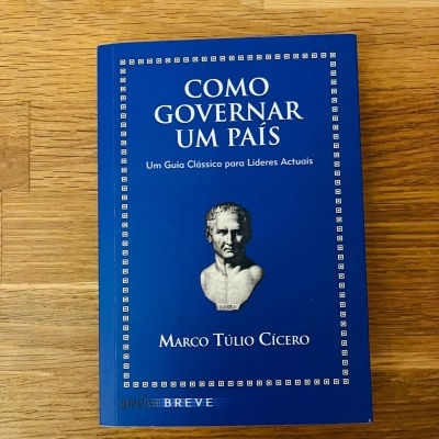 Livro azul 'Como Governar um País' com busto branco, sobre mesa de madeira clara