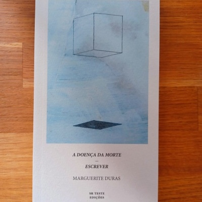 Livro 'A DOENÇA DA MORTE ESCREVER' de Marguerite Duras com capa branca e ilustração de cubo suspenso