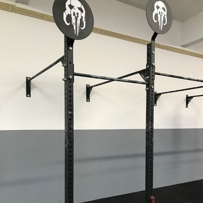 Estrutura metálica preta para treino com discos pretos decorativos numa parede branca e cinza