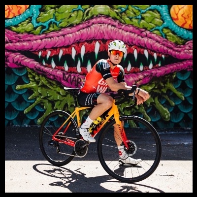 Ciclista com bicicleta amarela em frente a mural colorido de boca aberta