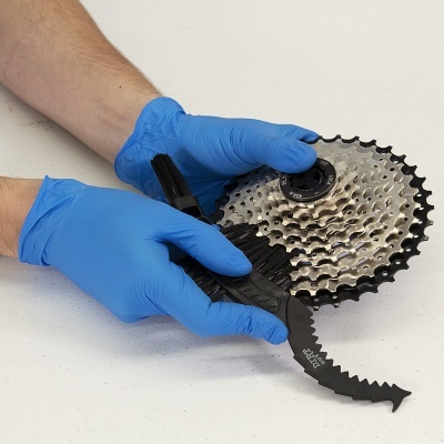 Mãos com luvas azuis seguram cassete de bicicleta e escova de limpeza preta