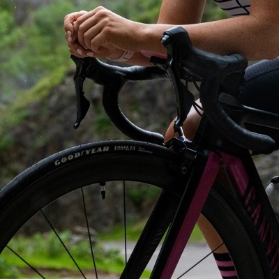 Bicicleta de estrada preta com detalhes roxos e pneus Goodyear Eagle F1 com pessoa segurando o guiador.