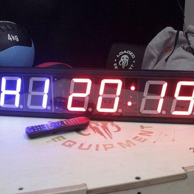 Relógio digital de parede com dígitos azuis e vermelhos, bola de 4kg e caixa com inscrição